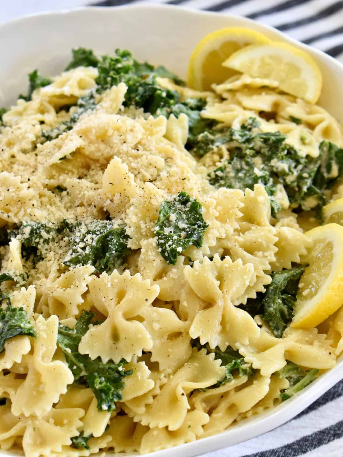 Kale Caesar Pasta Salad in a white bowl with lemon wedges.