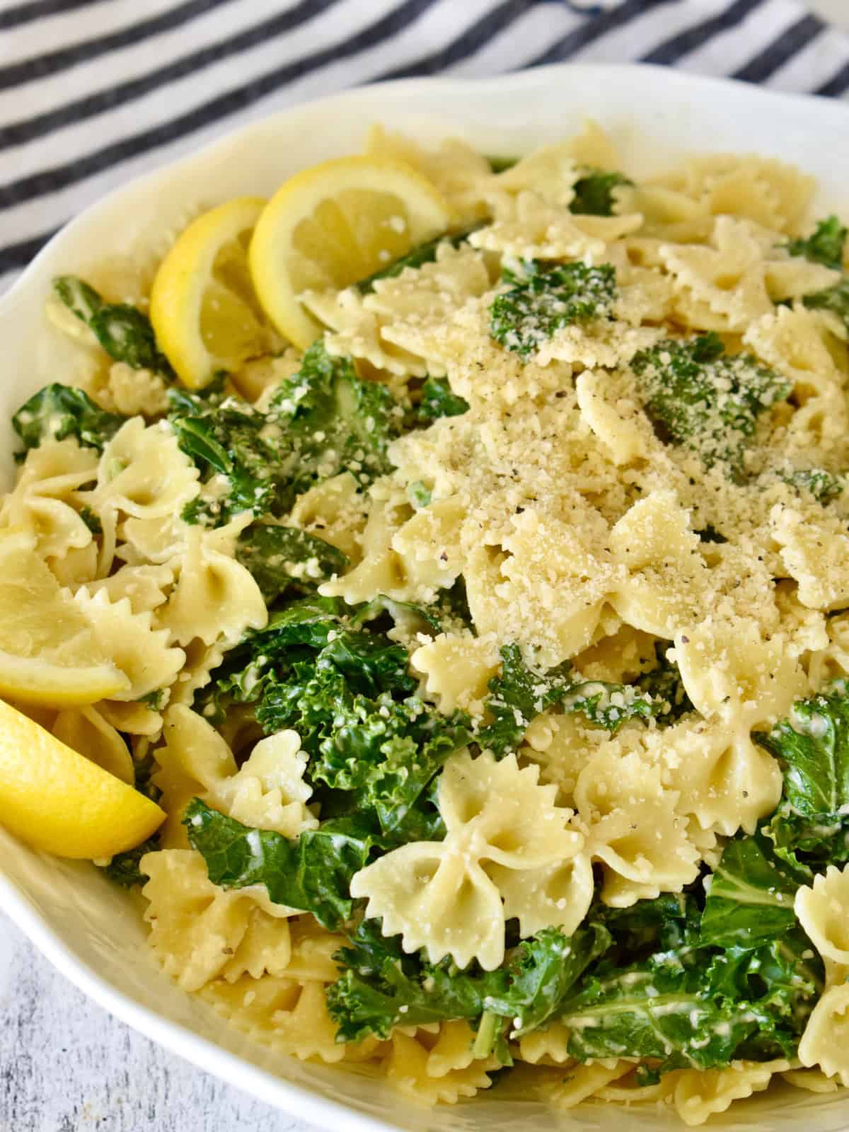Kale Caesar Pasta Salad in a white bowl with lemon slices.