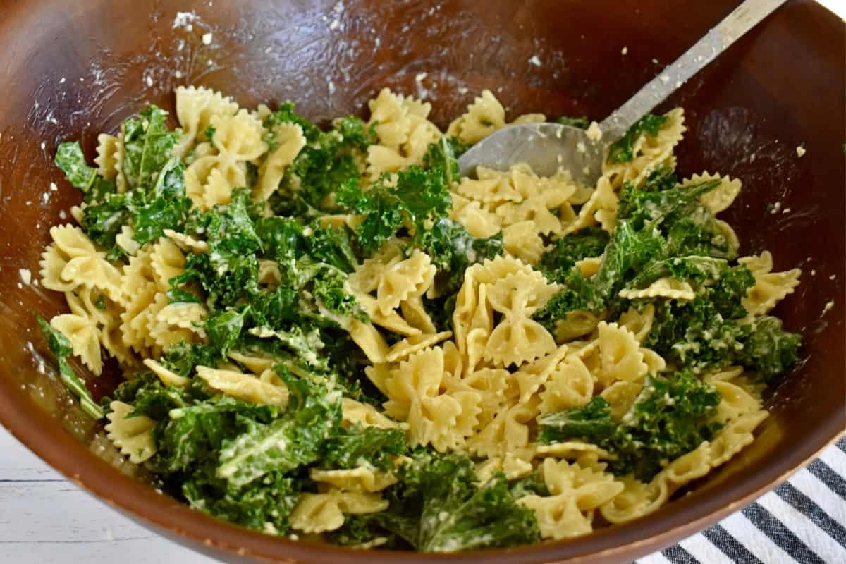 Pasta tossed with kale and dressing a large wooden bowl.