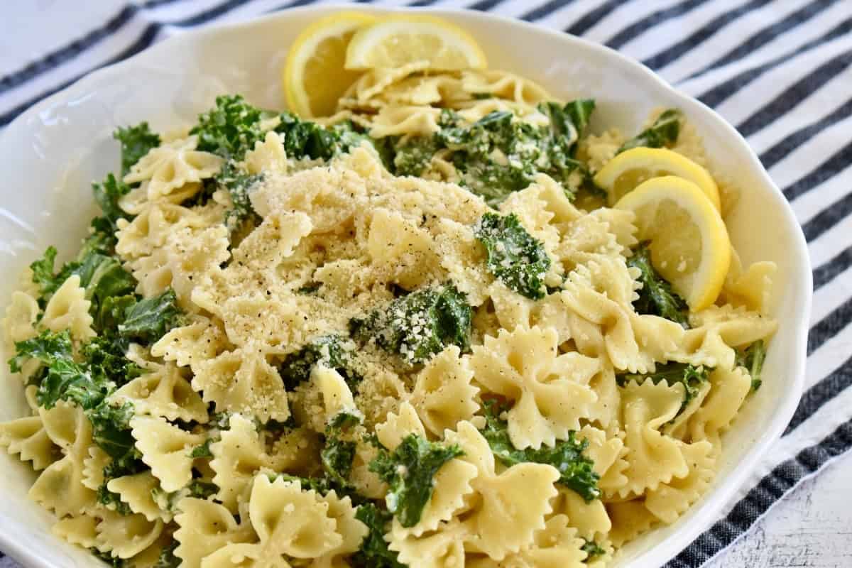 Kale Caesar Pasta Salad in a large white serving bowl with lemon slices.