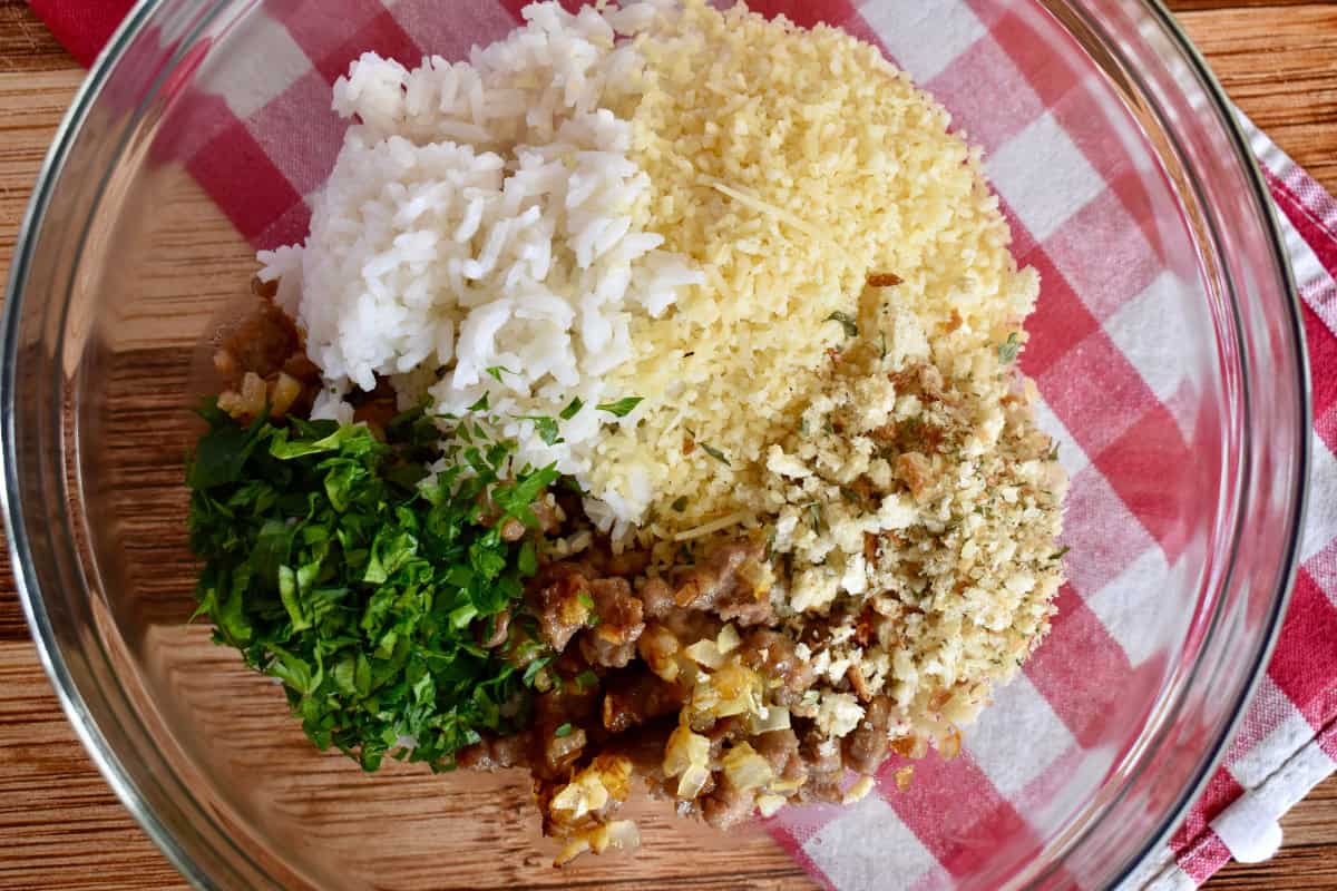 Filling ingredients in a bowl including cooked sausage, rice, Parmesan, and breadcrumbs.