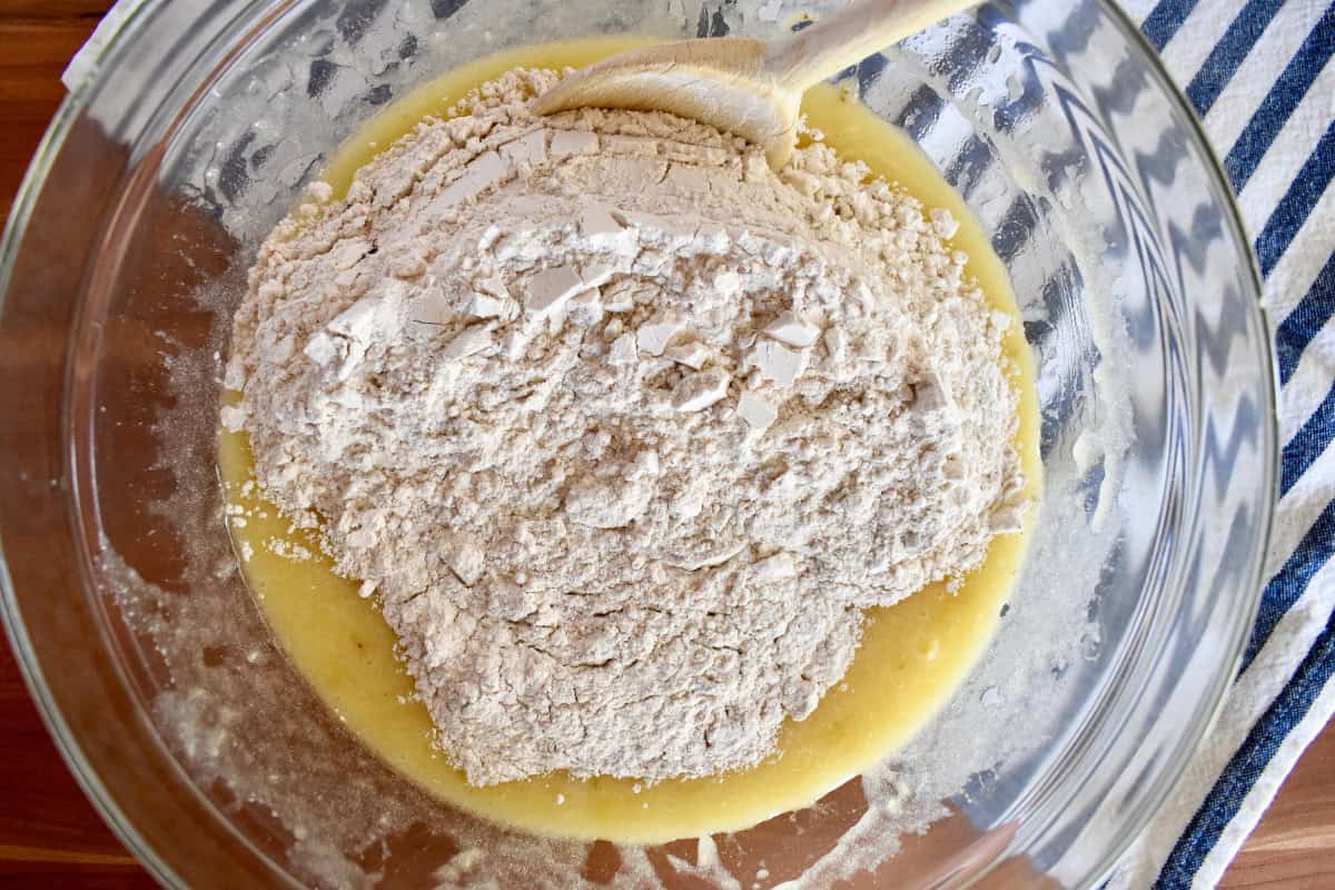 Dry ingredients poured into wet ingredients with a wood spoon in the bowl.